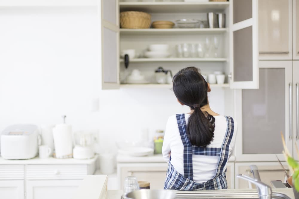 収納棚の戸を開けて考え込んでいる女性