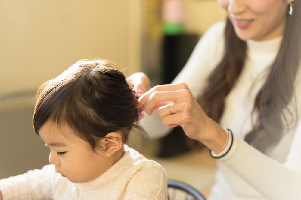 子どもの髪の毛を結んでいる女性